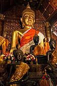 Wat Xieng Thong temple in Luang Prabang, Laos.  The main Buddha of the sim sits on a platform, surrounded by smaller statues, candles, and offerings. 